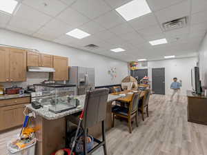 Kitchen with light stone countertops, a center island with sink, stainless steel appliances, a drop ceiling, and a breakfast bar area