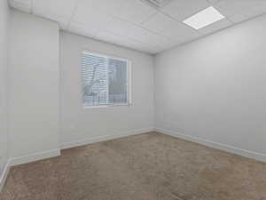 Carpeted room featuring a drop ceiling with recessed lighting, a window with horizontal blinds, and neutral wall tones