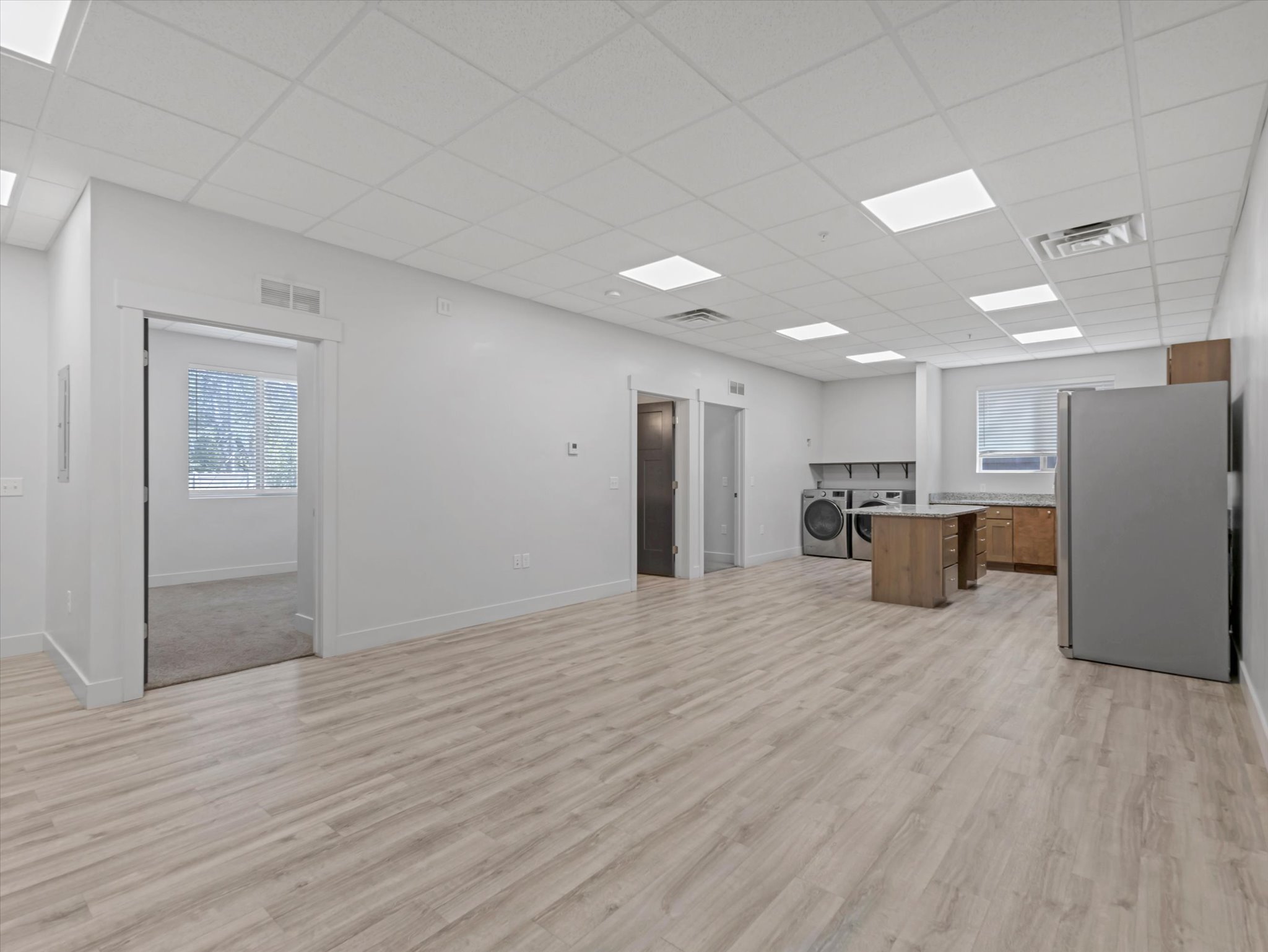 Open-concept living space featuring wood-finish flooring throughout, a modern kitchen area with a refrigerator and wood cabinetry, and an in-unit washer and dryer