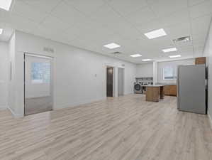 Open-concept living space featuring wood-finish flooring throughout, a modern kitchen area with a refrigerator and wood cabinetry, and an in-unit washer and dryer