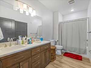Bathroom featuring double vanity, shower / tub combo, and light wood-style flooring