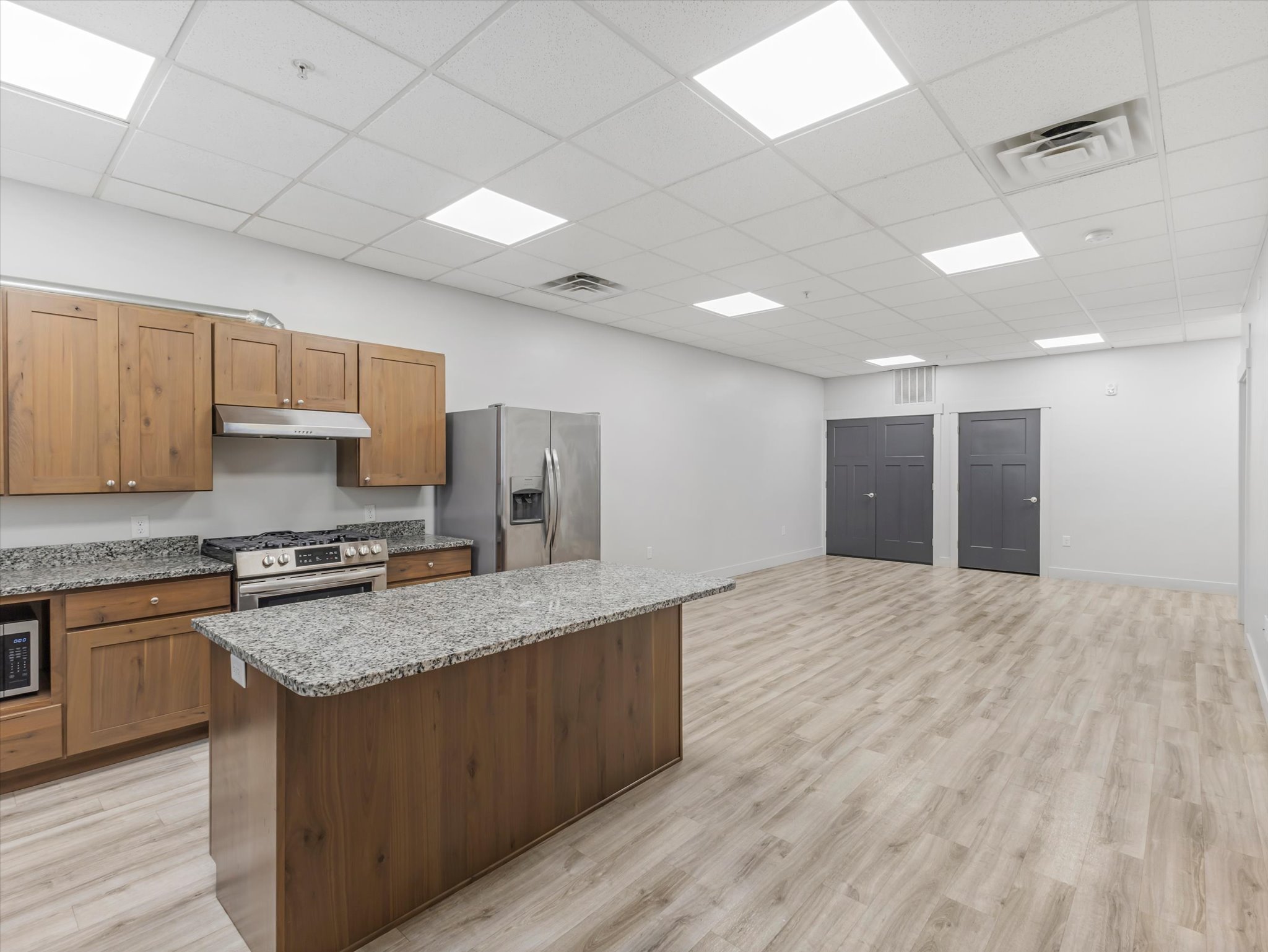 Open-concept kitchen featuring wood-finish cabinetry, light-toned countertops, a stainless steel gas range with a matching range hood, and a large central island