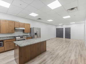 Open-concept kitchen featuring wood-finish cabinetry, light-toned countertops, a stainless steel gas range with a matching range hood, and a large central island