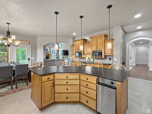 Kitchen with arched walkways, hanging lights, a kitchen island, and dark countertops