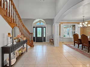 Entrance foyer with hanging lights, arched walkways, decorative columns, light tile patterned flooring, and a high ceiling
