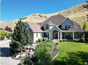 View of front of home featuring stone siding, covered porch, a front lawn, a mountain view, and roof with shingles