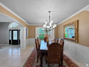 Formal dining room featuring decorative columns, wainscoting, a decorative wall, arched walkways, and a chandelier