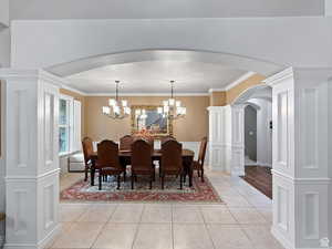 Formal dining room with ornate columns, arched walkways, light tile patterned floors, ornamental molding, and suspended lighting