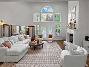 Great room  with a glass covered fireplace, wood finished floors, healthy amount of natural light, a high ceiling, and french doors