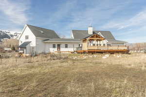 Rear view of property featuring a deck with mountain view, a chimney, a shingled roof, and an outbuilding