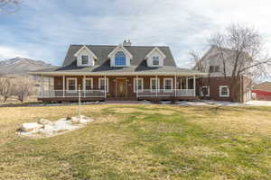 Farmhouse-style home featuring covered porch, a front lawn, brick siding, a chimney, and a shingled roof