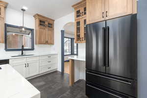 Kitchen with high quality fridge, arched walkways, light stone counters, glass insert cabinets, and dark wood-style floors