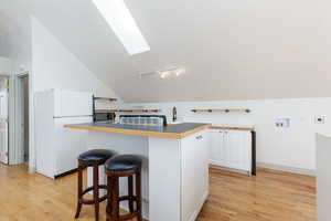 Kitchen with a skylight, vaulted ceiling, freestanding refrigerator, white cabinetry, and a breakfast bar
