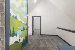 Corridor featuring dark colored carpet and vaulted ceiling
