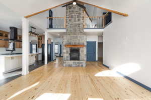 Unfurnished living room with a ceiling fan, a stone fireplace, arched walkways, light wood-style flooring, and lofted ceiling