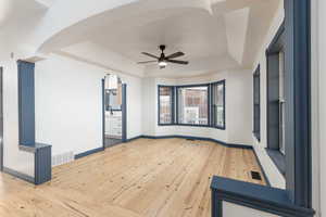 Dining room with a raised ceiling, light wood-style floors, a ceiling fan, and arched walkways