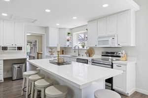 Kitchen with a kitchen bar, open shelves, white cabinetry, stainless steel appliances, and recessed lighting