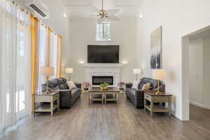 Living area featuring crown molding, a fireplace, ceiling fan, dark wood-style floors, and a high ceiling