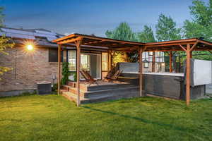 Back of house with a hot tub, a lawn, a deck, and brick siding
