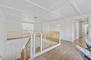 Hallway featuring wood finished floors, an upstairs landing, a decorative wall, ornamental molding, and suspended lighting