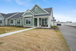 View of front of house with board and batten siding, covered porch, roof with shingles, a front yard, and asphalt driveway