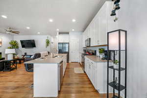 Kitchen with white cabinets, stainless steel appliances, a ceiling fan, an island with sink, and light countertops