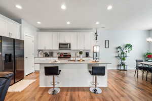 Kitchen featuring stainless steel appliances, white cabinetry, light wood finished floors, and an island with sink