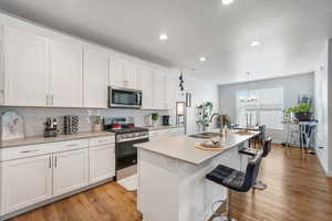 Kitchen featuring white cabinetry, stainless steel appliances, an island with sink, a kitchen bar, and light wood-type flooring