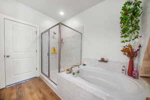 Bathroom featuring a marble finish shower, a garden tub, and wood finished floors