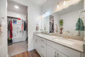 Full bathroom with double vanity, a walk in closet, and light wood-style floors