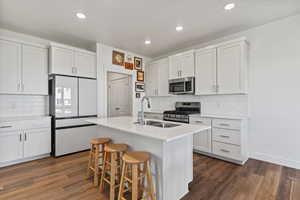 Kitchen featuring stainless steel appliances, dark wood finished floors, white cabinets, backsplash, and a breakfast bar