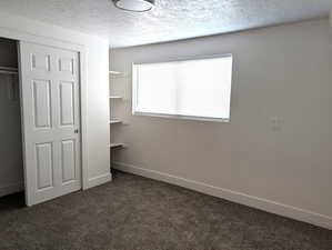 Unfurnished bedroom with a closet, dark colored carpet, and a textured ceiling