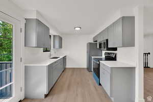 Kitchen featuring gray cabinets, stainless steel appliances, light wood-style flooring, and light stone countertops