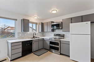 Kitchen with stainless steel appliances, gray cabinets, backsplash, and light flooring