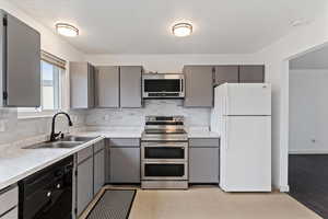 Kitchen featuring gray cabinetry, stainless steel appliances, light countertops, and backsplash