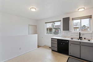 Kitchen featuring light floors, gray cabinets, light countertops, dishwasher, and backsplash