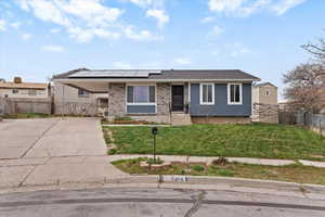 View of front facade featuring solar panels, driveway, an attached carport, brick siding, and a shingled roof