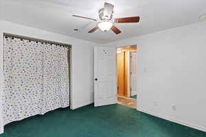Unfurnished bedroom with a ceiling fan, dark colored carpet, and a closet