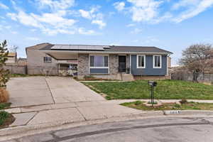 View of front of property featuring roof mounted solar panels, driveway, a carport, brick siding, and roof with shingles
