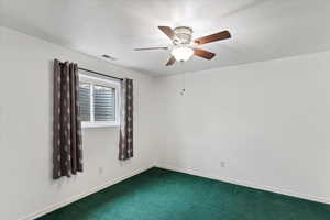 Empty room featuring ceiling fan and dark carpet
