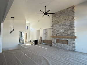 Unfurnished living room with a stone fireplace, a high ceiling, and a ceiling fan