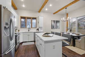 Kitchen featuring stainless steel appliances, white cabinets, light stone countertops, tasteful backsplash, and beamed ceiling