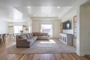 Living area featuring a tray ceiling, light wood-style floors, a textured ceiling, and suspended lighting
