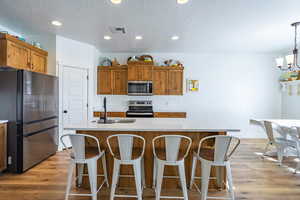 Kitchen featuring stainless steel appliances, a kitchen breakfast bar, wood finish cabinets, light wood-style floors, and a textured ceiling