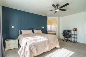 Bedroom with carpet floors, an office area, wooden walls, a ceiling fan, and connected bathroom