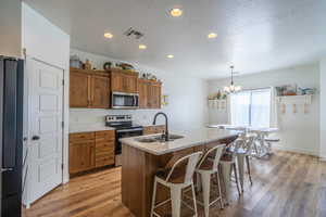 Kitchen featuring stainless steel appliances, wood finish cabinets, a breakfast bar area, a center island with sink, and a textured ceiling