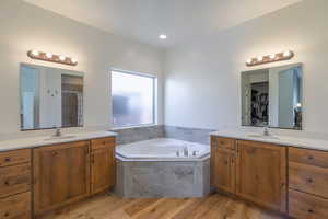 Bathroom featuring two vanities, light wood finished floors, a garden tub, and a stall shower