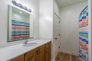 Full bath with vanity, a shower with shower curtain, and light wood-style flooring