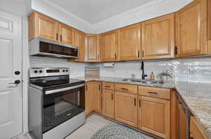 Kitchen with stainless steel appliances, light stone counters, decorative backsplash, and ornamental molding