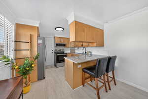 Kitchen featuring a peninsula, stainless steel appliances, a kitchen bar, crown molding, and light stone countertops